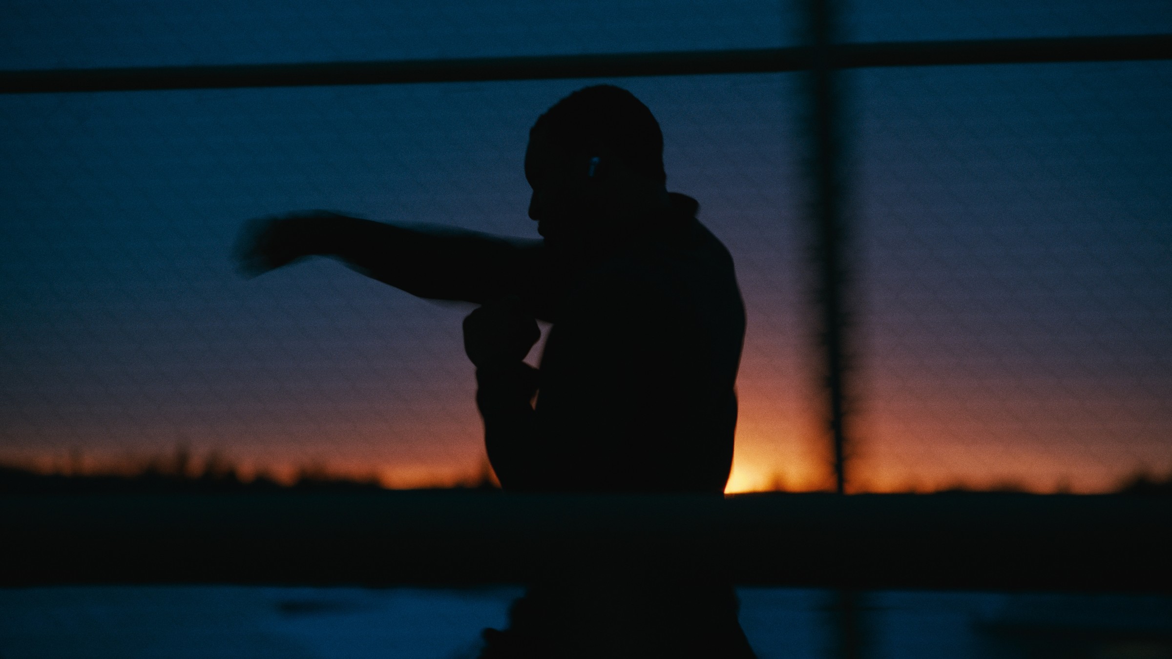 A boxer's silhouette throws a punch against a blue and orange evening sky — Kinetic