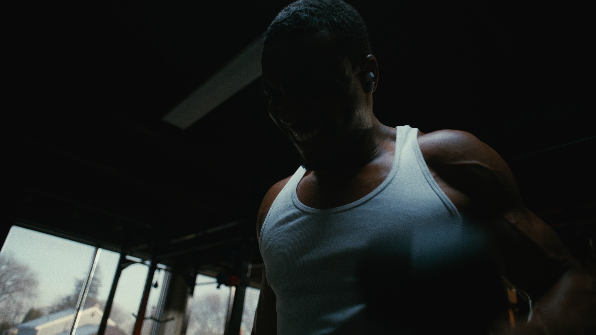An athlete in a white tank top stands in a dim gym — Kinetic