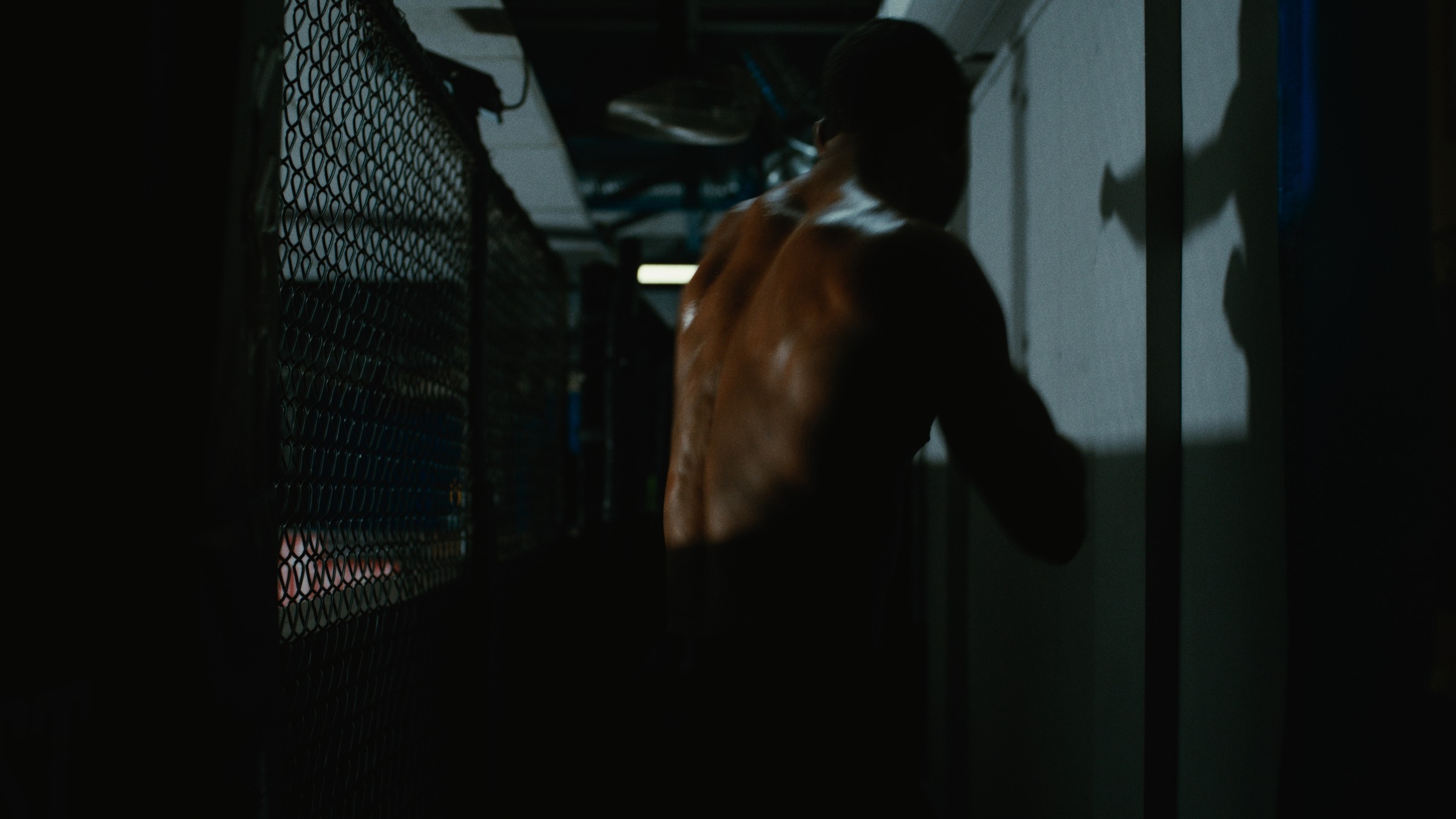 A shirtless boxer rests his arm on a training cage — Kinetic