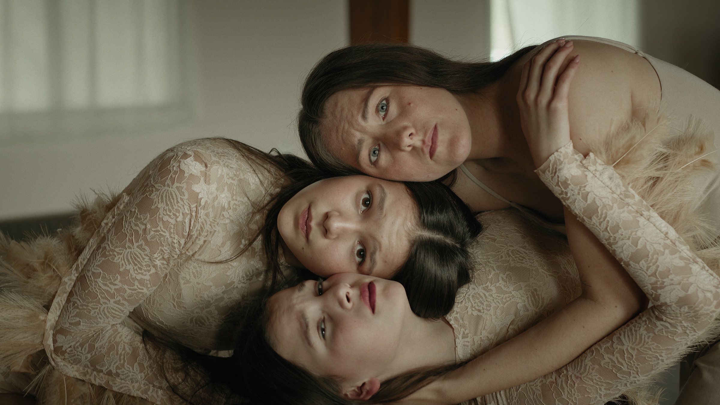 Three women rest their heads together in soft window light — Let Go