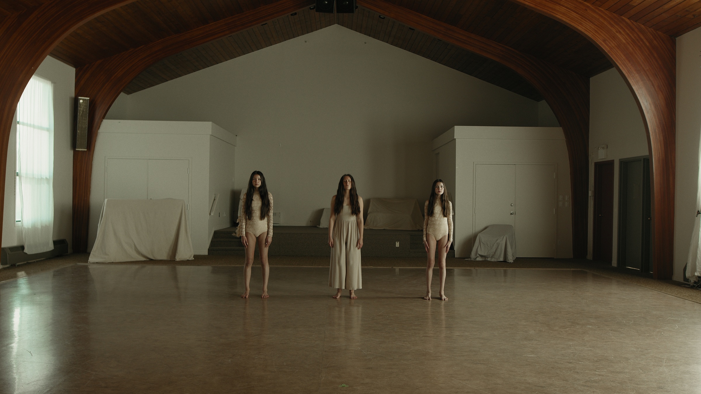 Three women stand beneath the curved wooden ceiling of a hall — Let Go