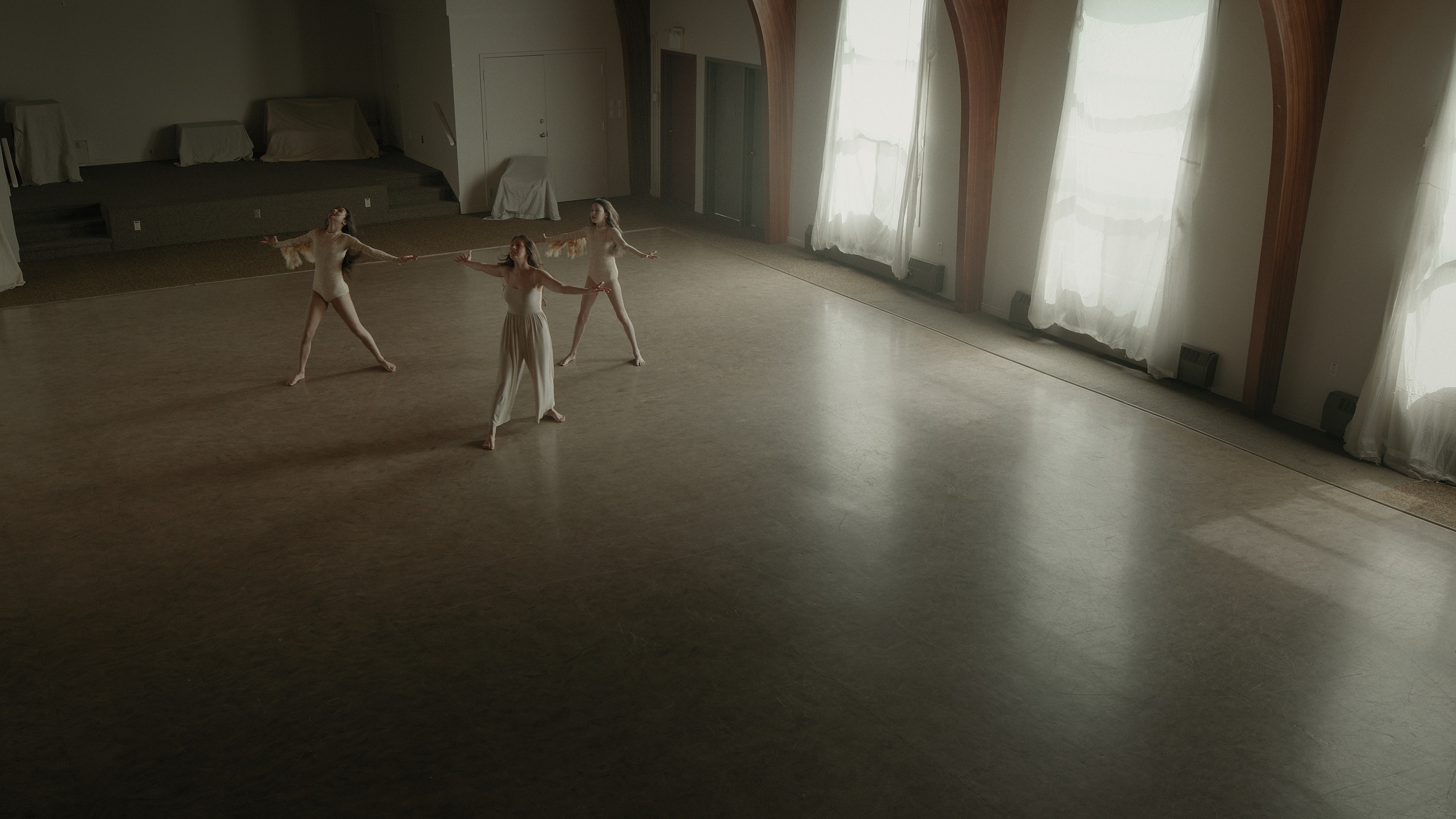 Three dancers extend their arms in a spacious hall beside tall windows — Let Go
