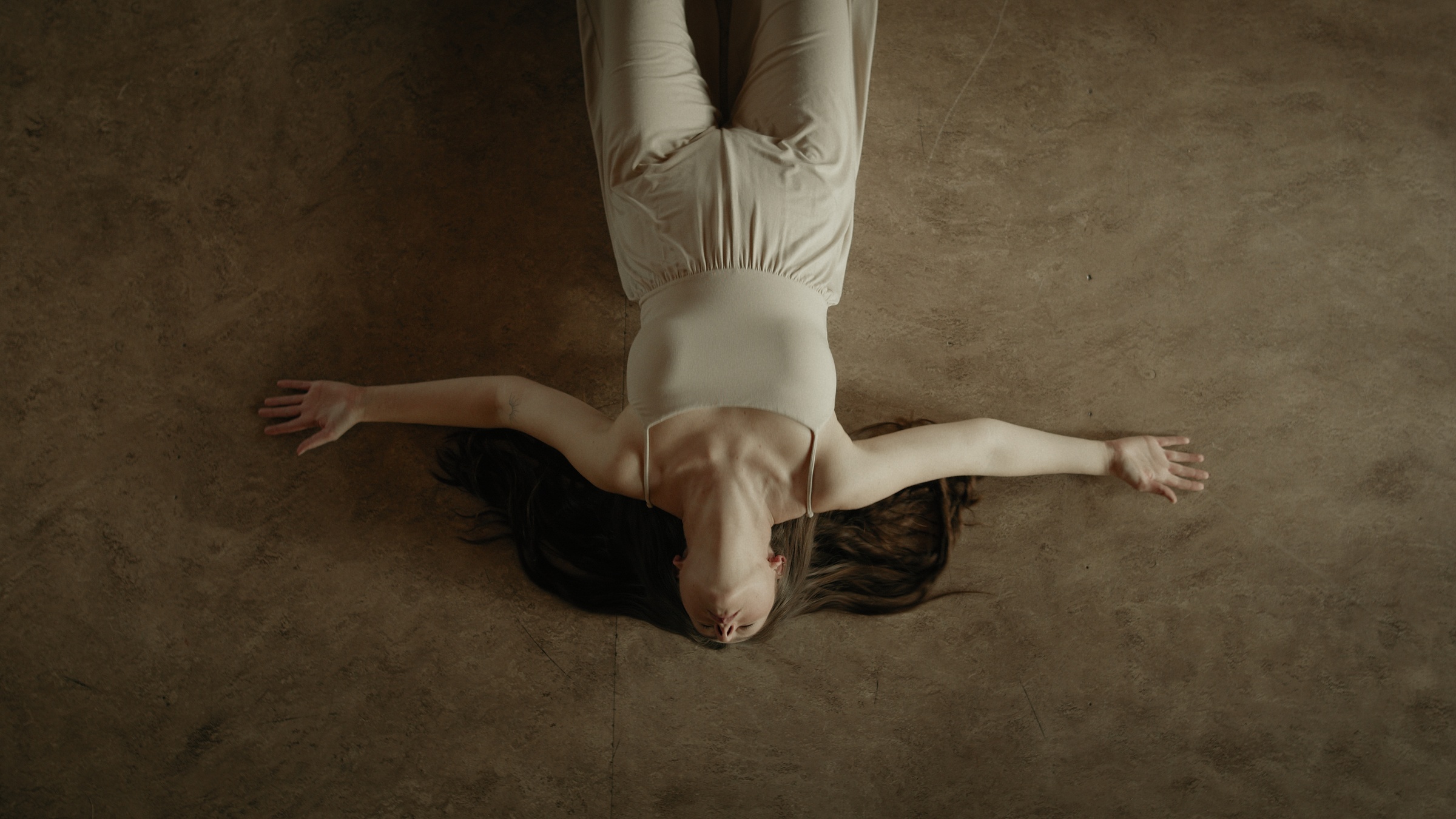 Overhead view of a woman lying on the wooden floor with her arms outstretched — Let Go
