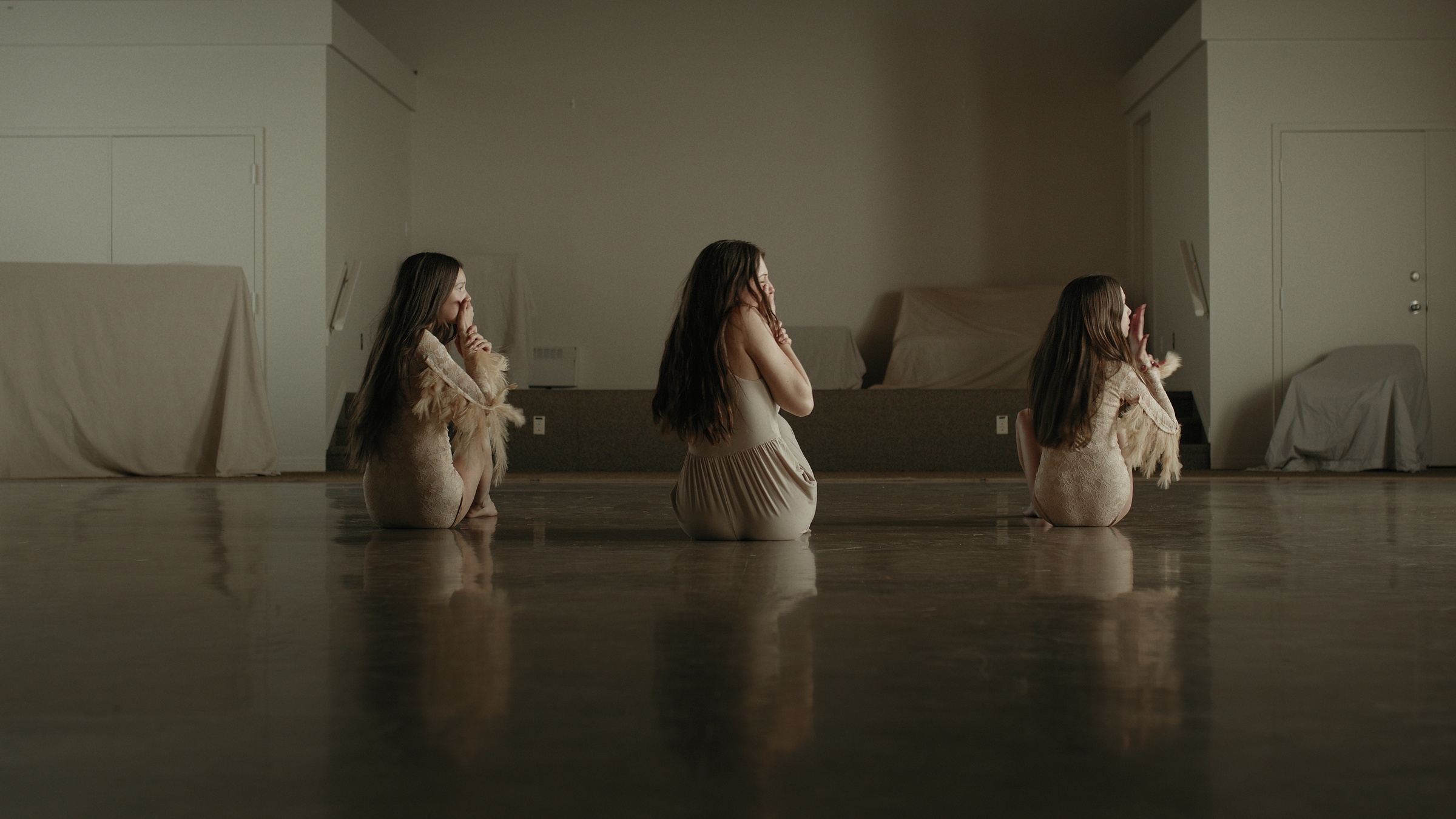 Three women kneel in a row on the reflective wooden floor — Let Go