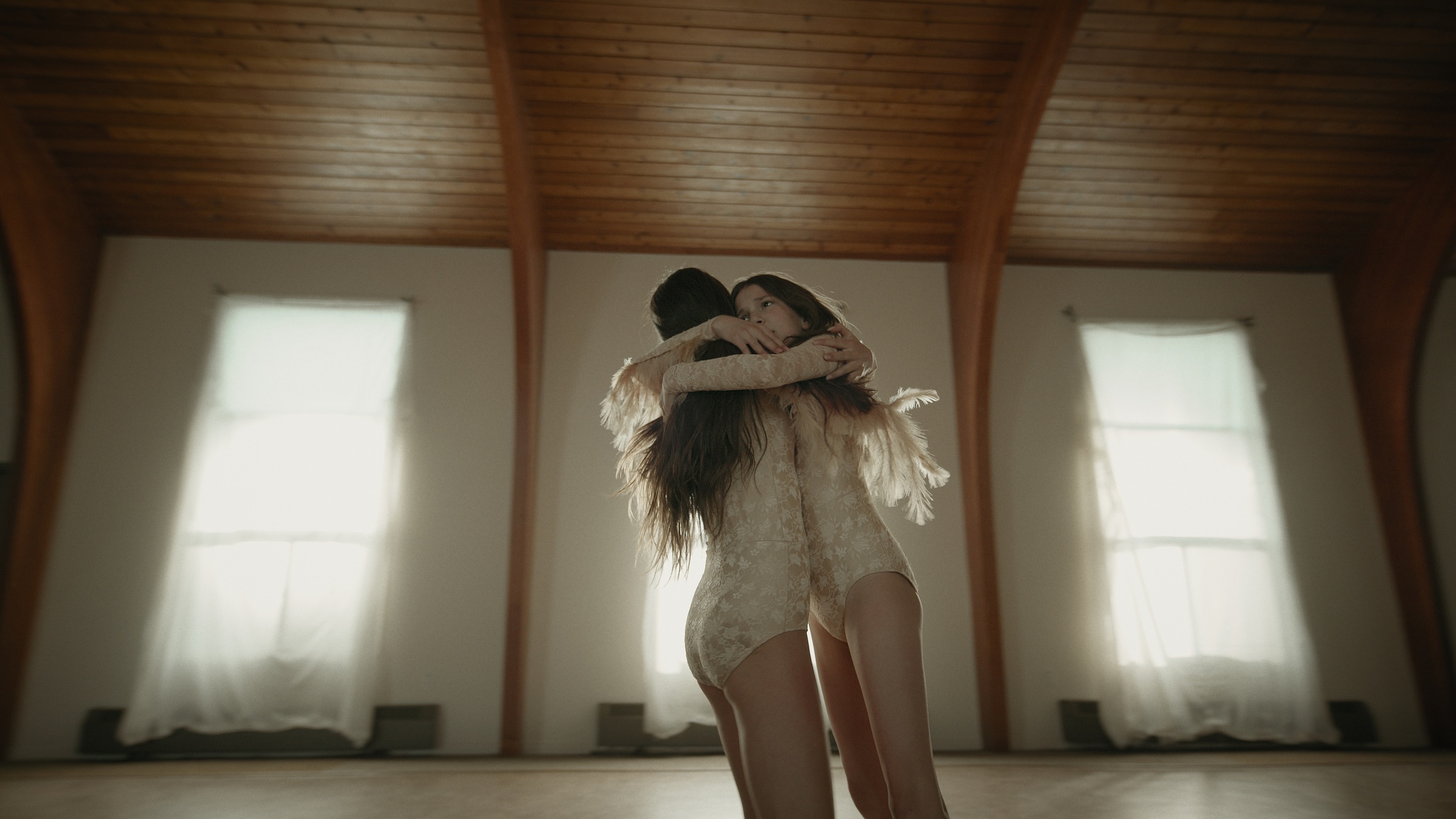 Two women embrace between softly lit windows — Let Go