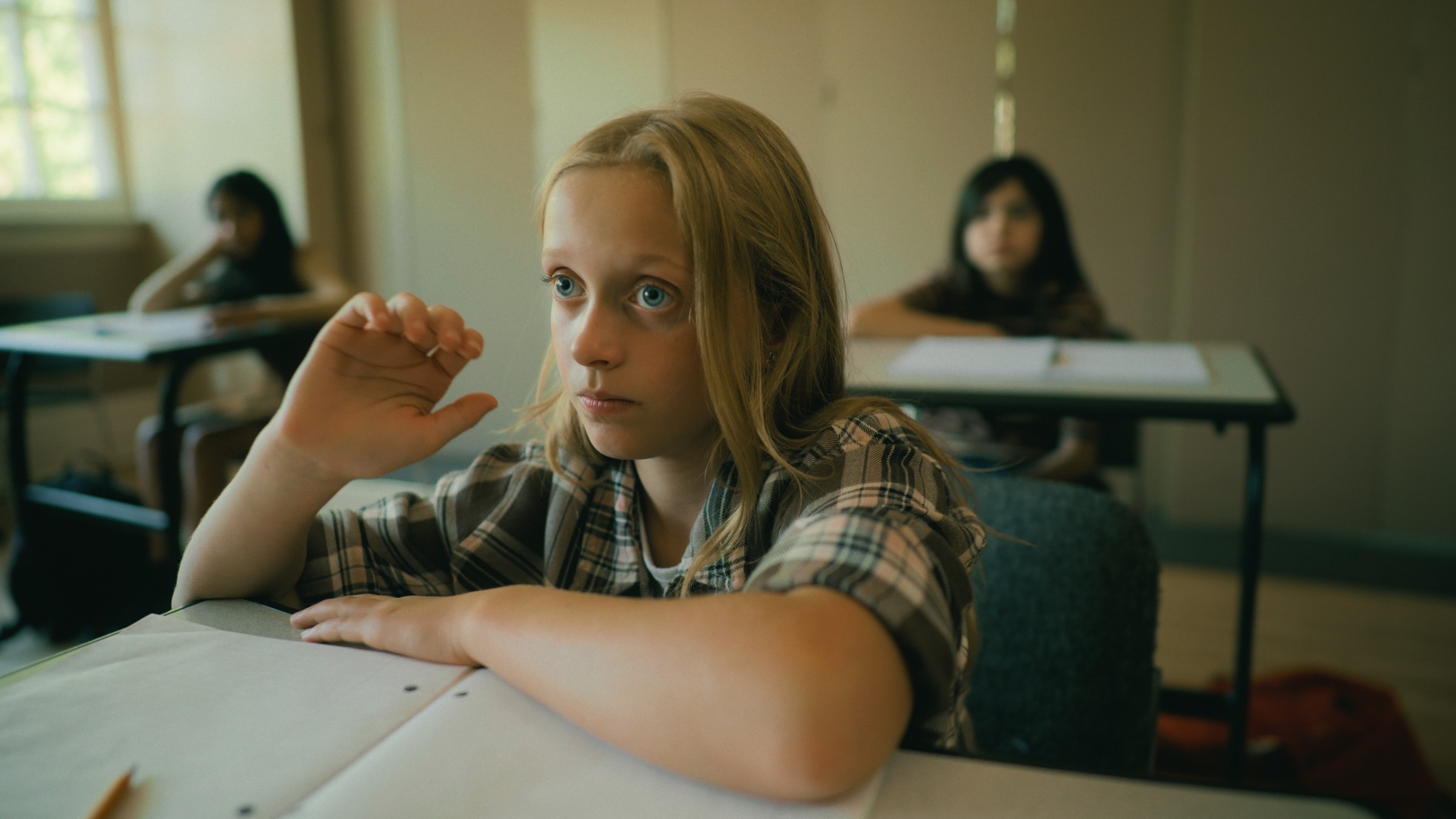 A blonde girl rests her hand near her face at a school desk — Little Fangs