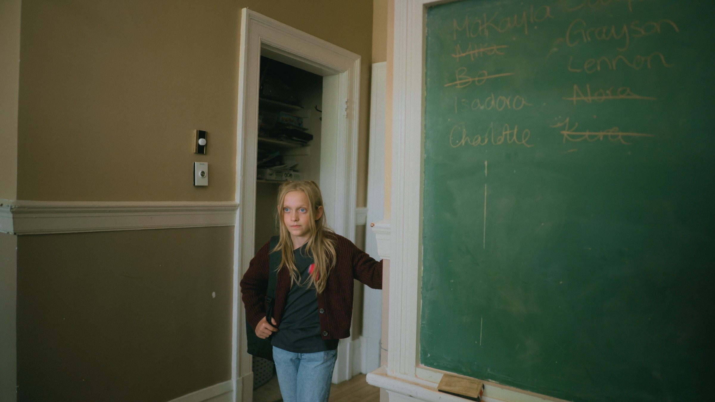 A girl stands beside a green classroom chalkboard — Little Fangs