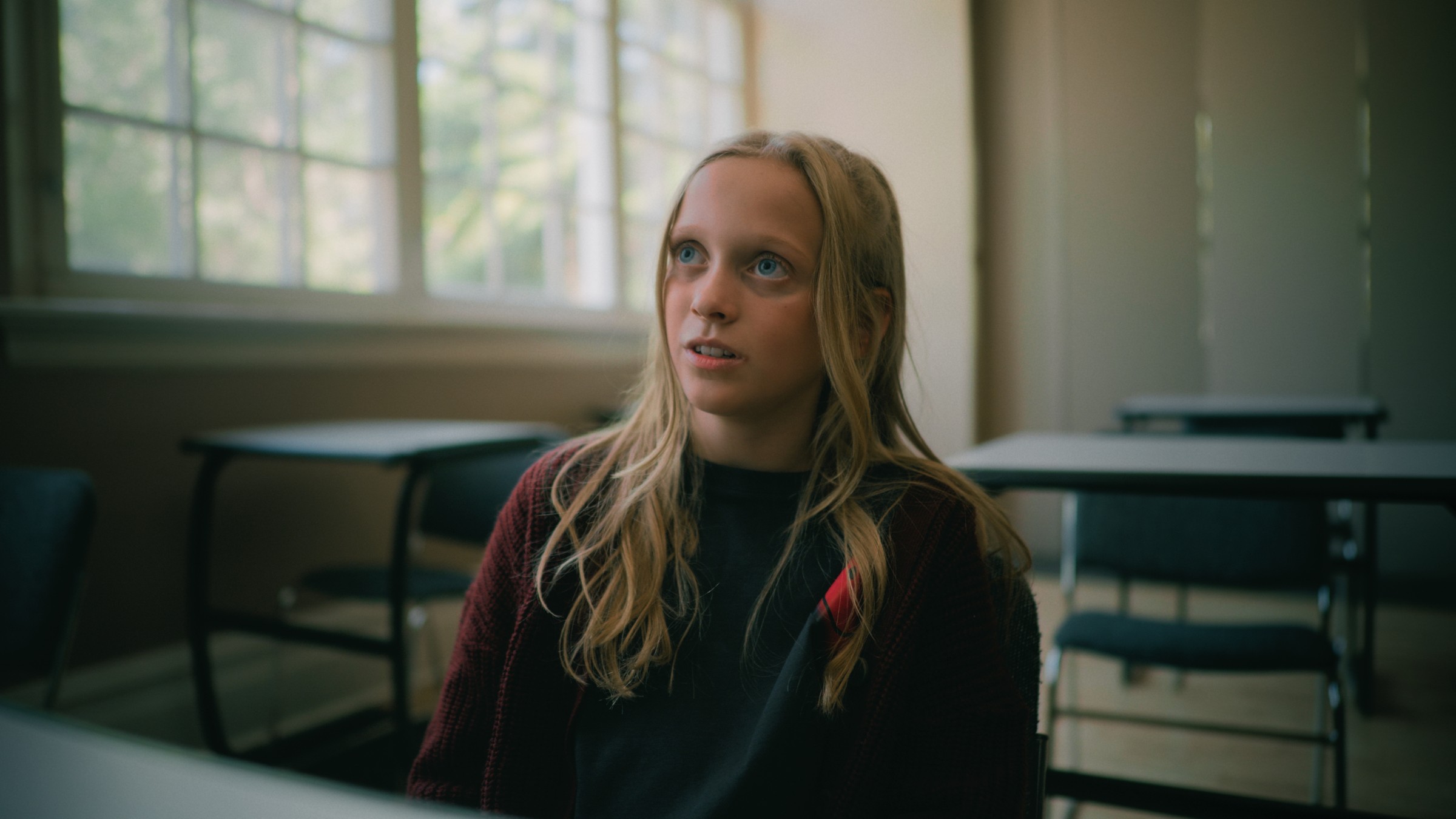 A blonde girl sits at a desk in a sunlit classroom — Little Fangs