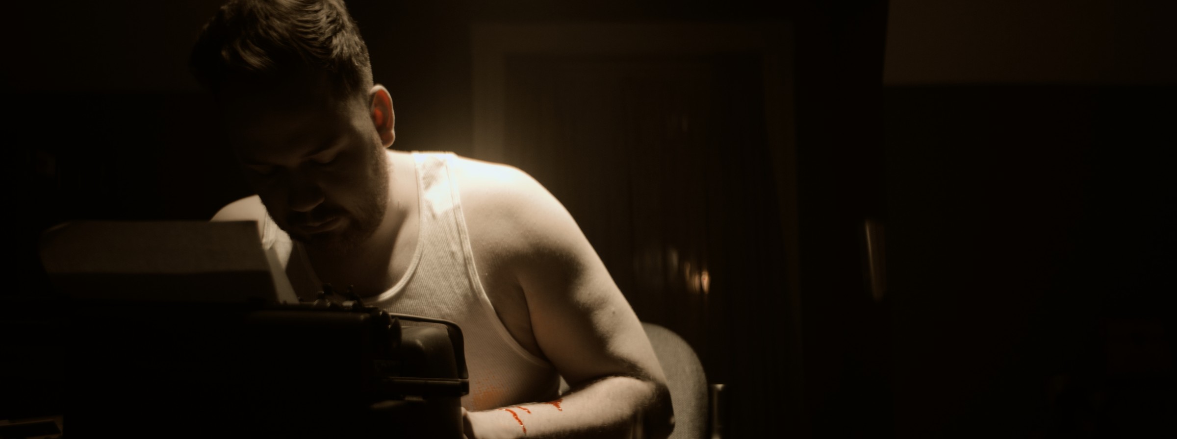 A man in a white shirt leans over a table in a dark room — Markings of Murder