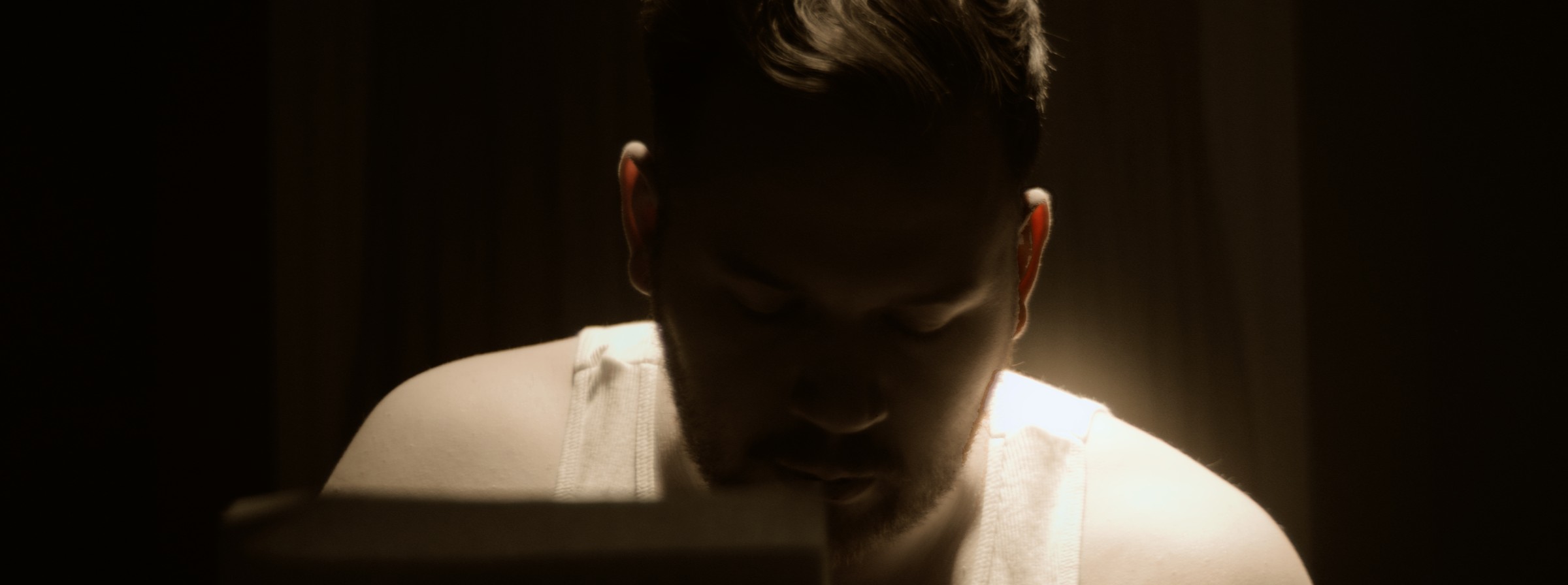 A man looks down beneath a warm overhead light — Markings of Murder