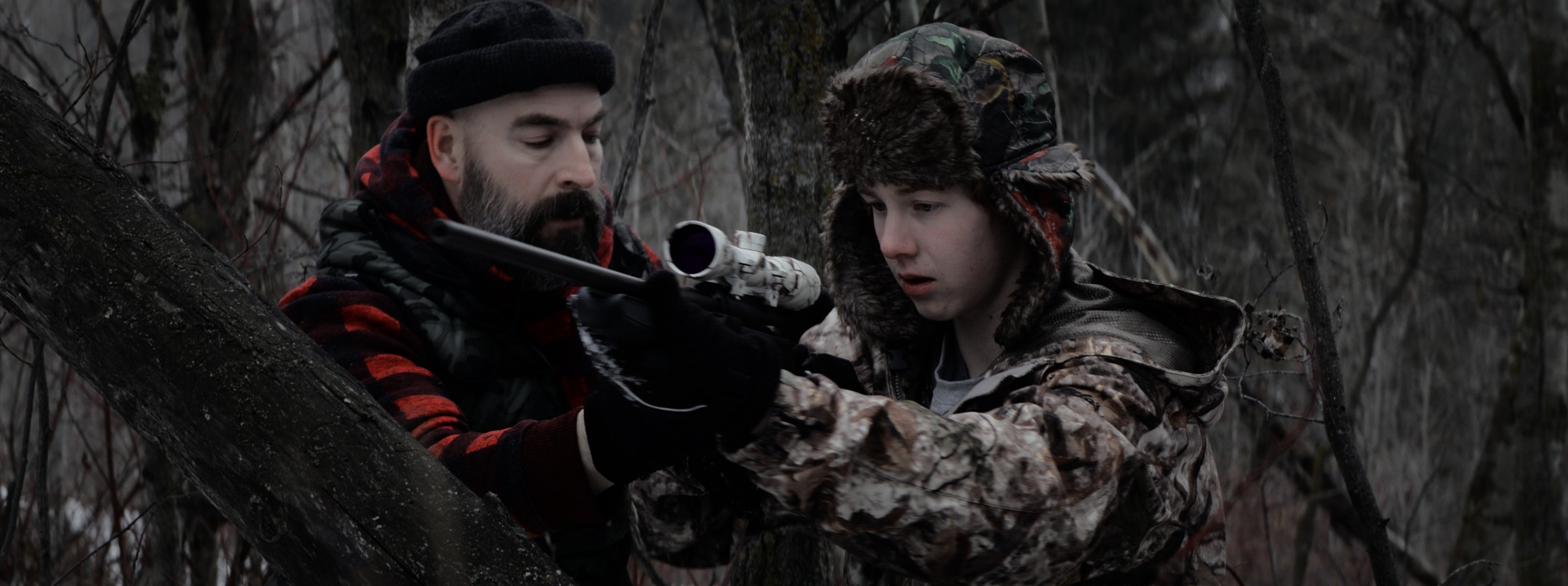 Two people handle a rifle in a leafless forest — Markings of Murder