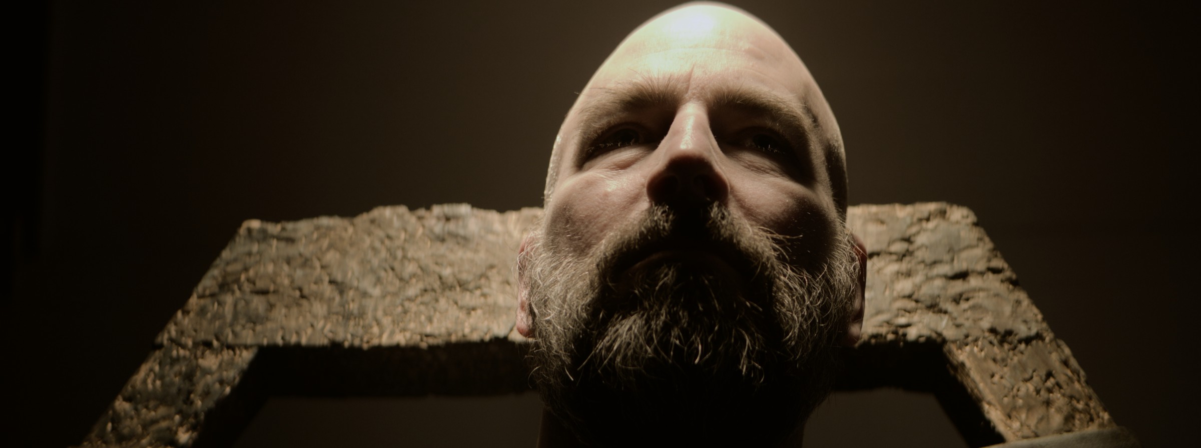 A bearded man reclines beneath a warm overhead light — Markings of Murder