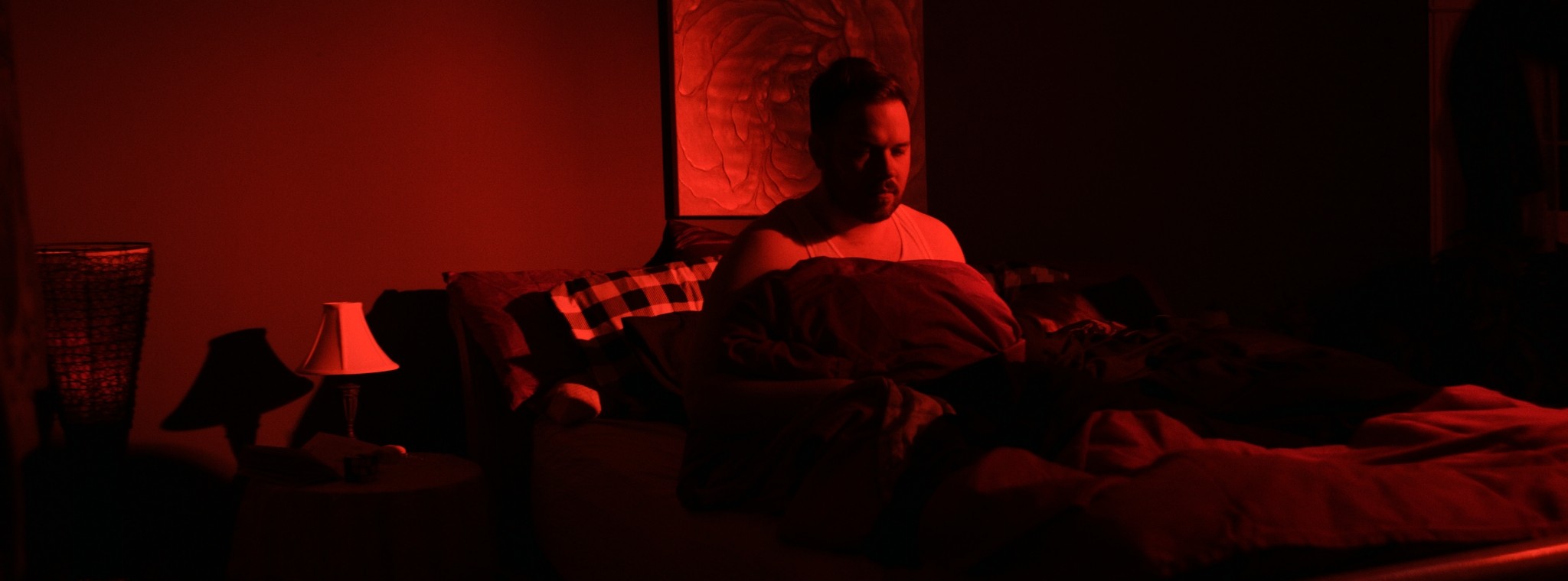 A man sits on a couch in a red-lit room — Markings of Murder