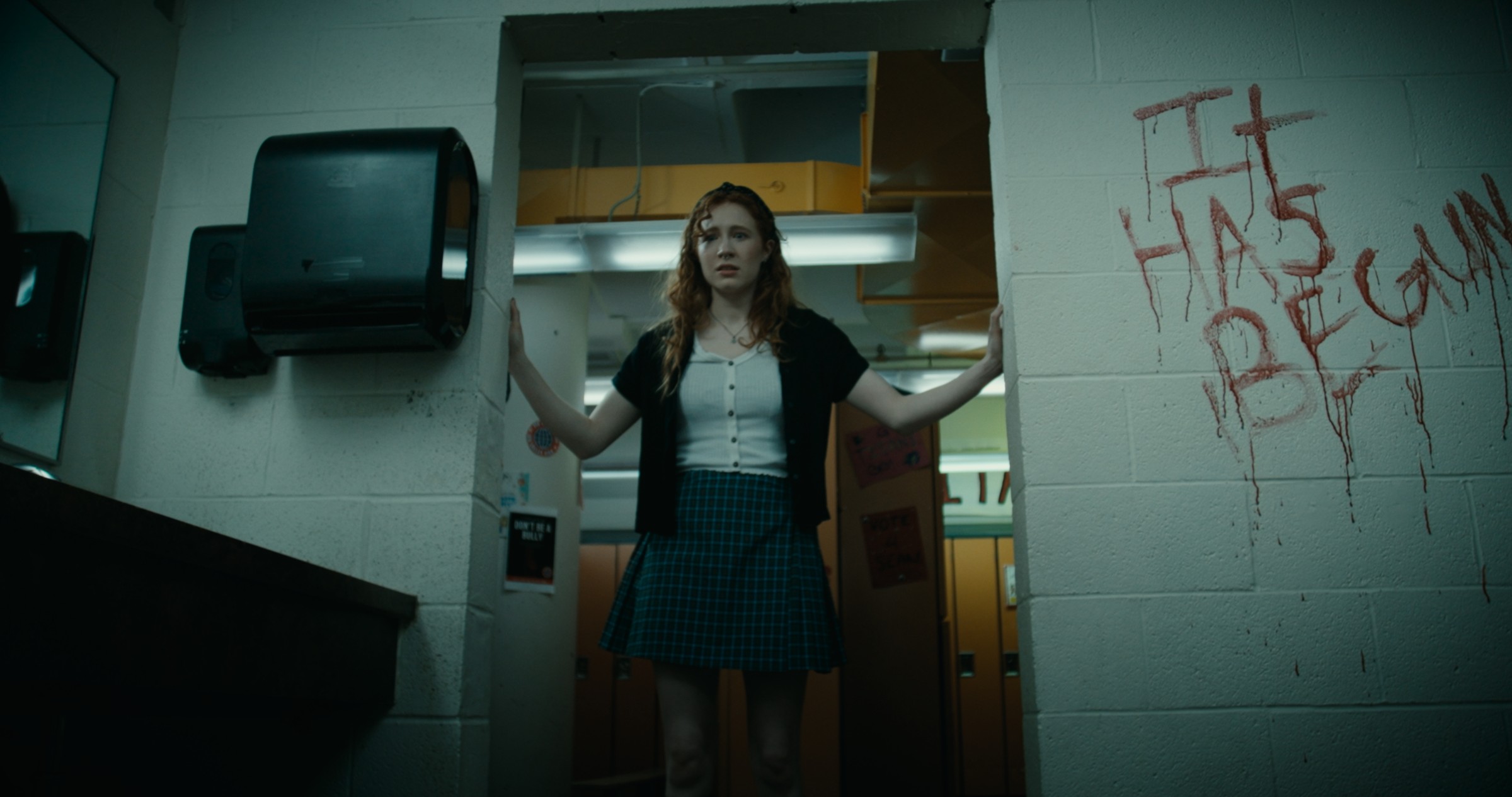 A woman stands in a dim corridor beside graffiti on a wall — Nemesis