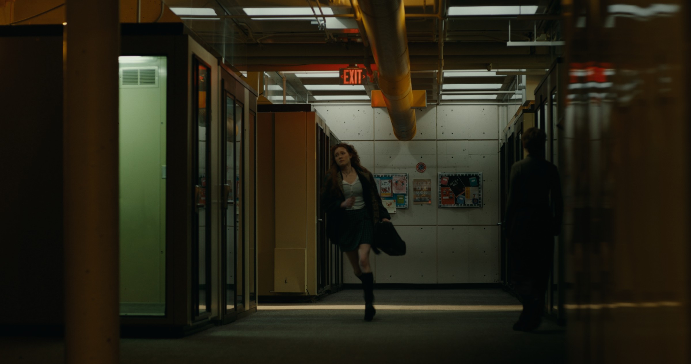 A woman moves through a dark corridor beneath exposed pipes — Nemesis