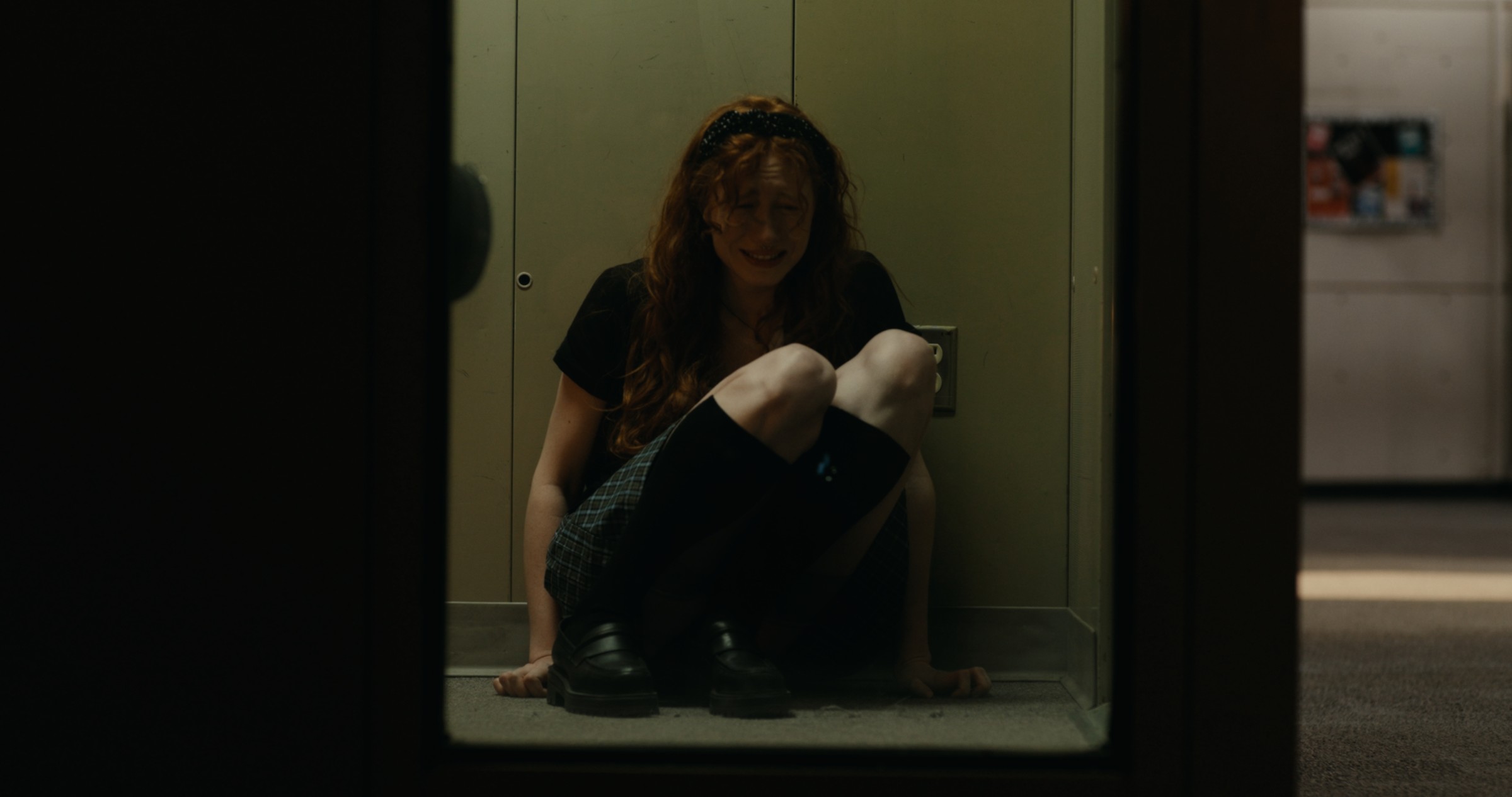 A woman sits on the floor in a dim doorway — Nemesis