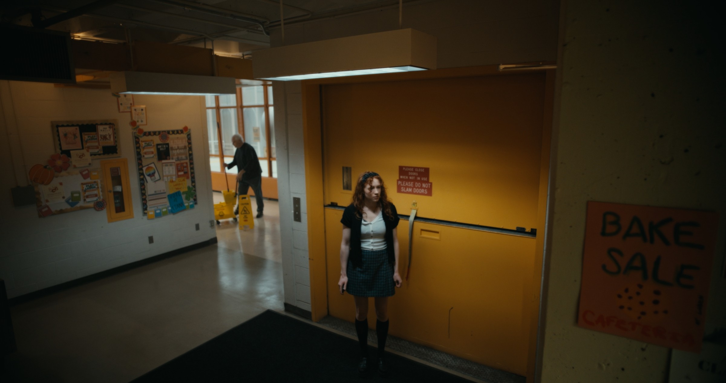 A woman stands beside a yellow door covered with warning signs — Nemesis