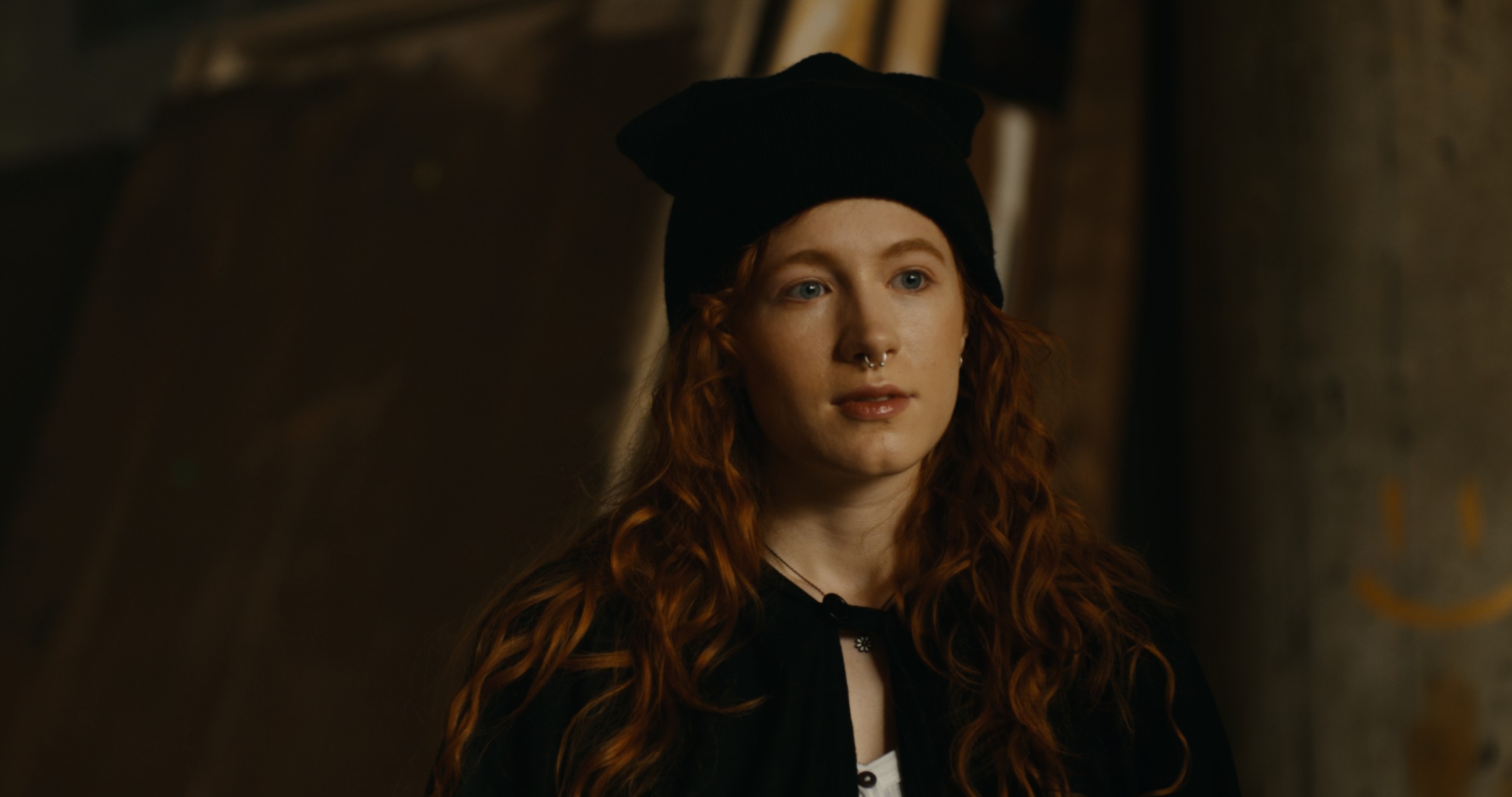 A woman wears a black cat-ear headband in a dim interior — Nemesis