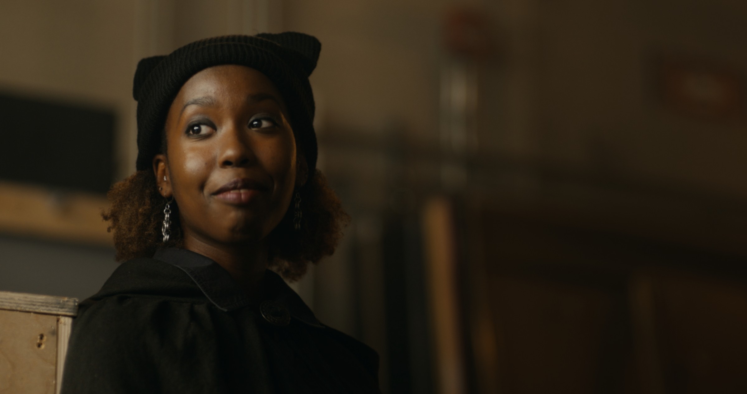 A woman in a black cat-ear headband looks upward — Nemesis