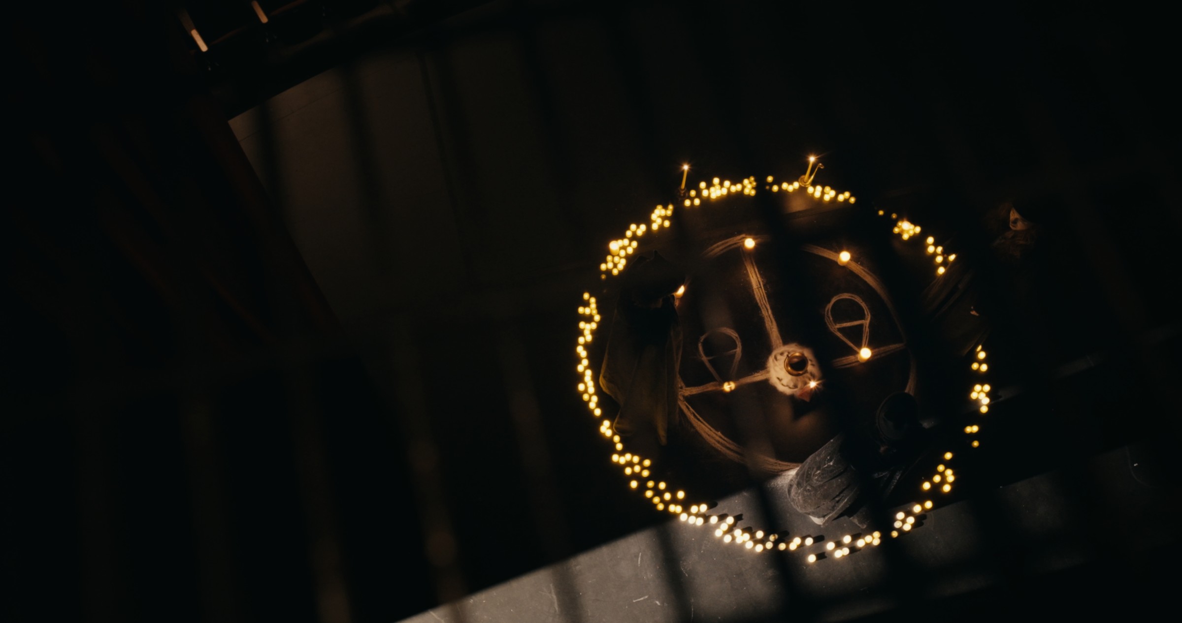 A face appears inside a glowing circle of sparks in the dark — Nemesis