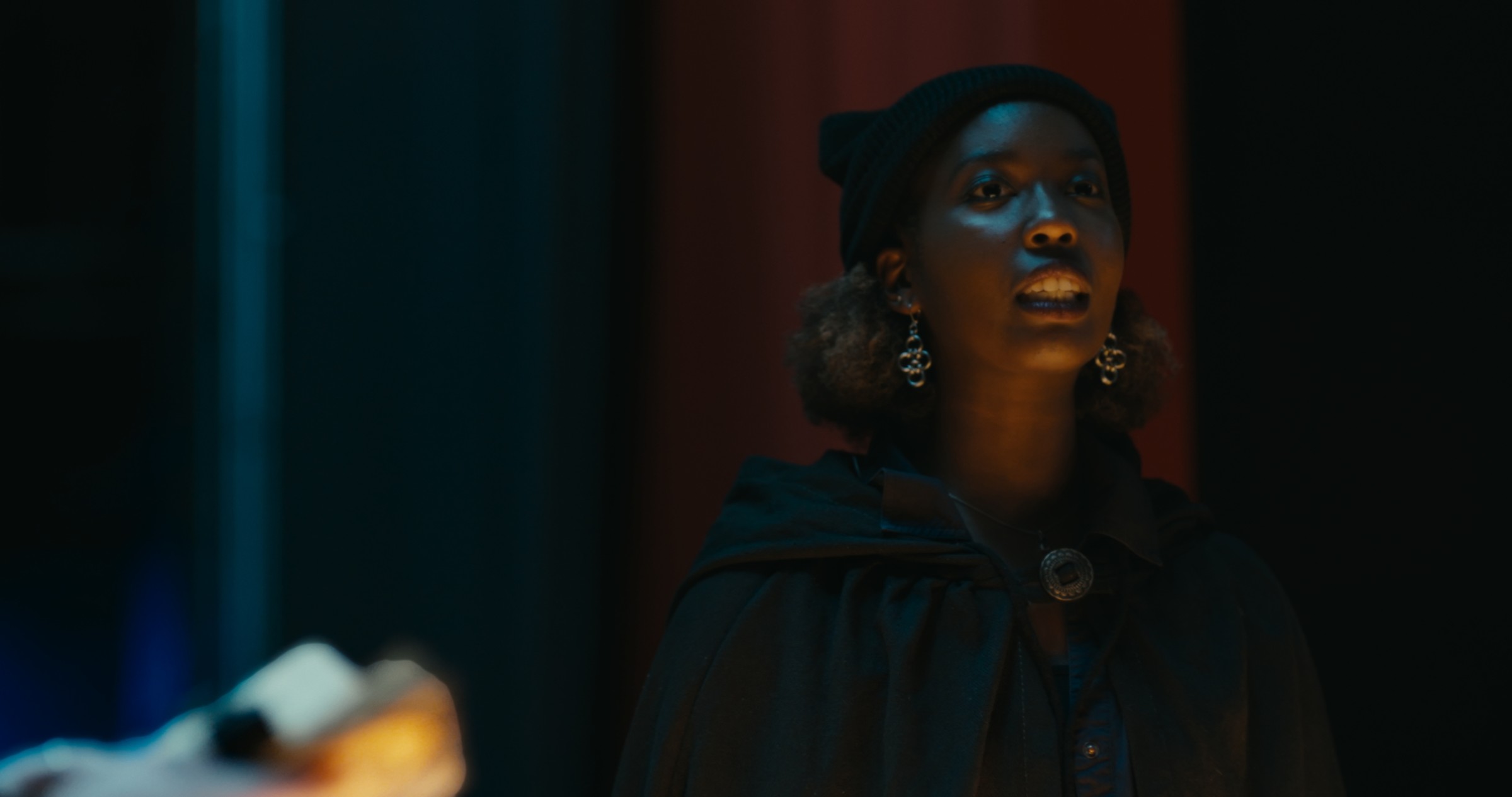 A woman stands in a dark doorway with blue light on her face — Nemesis