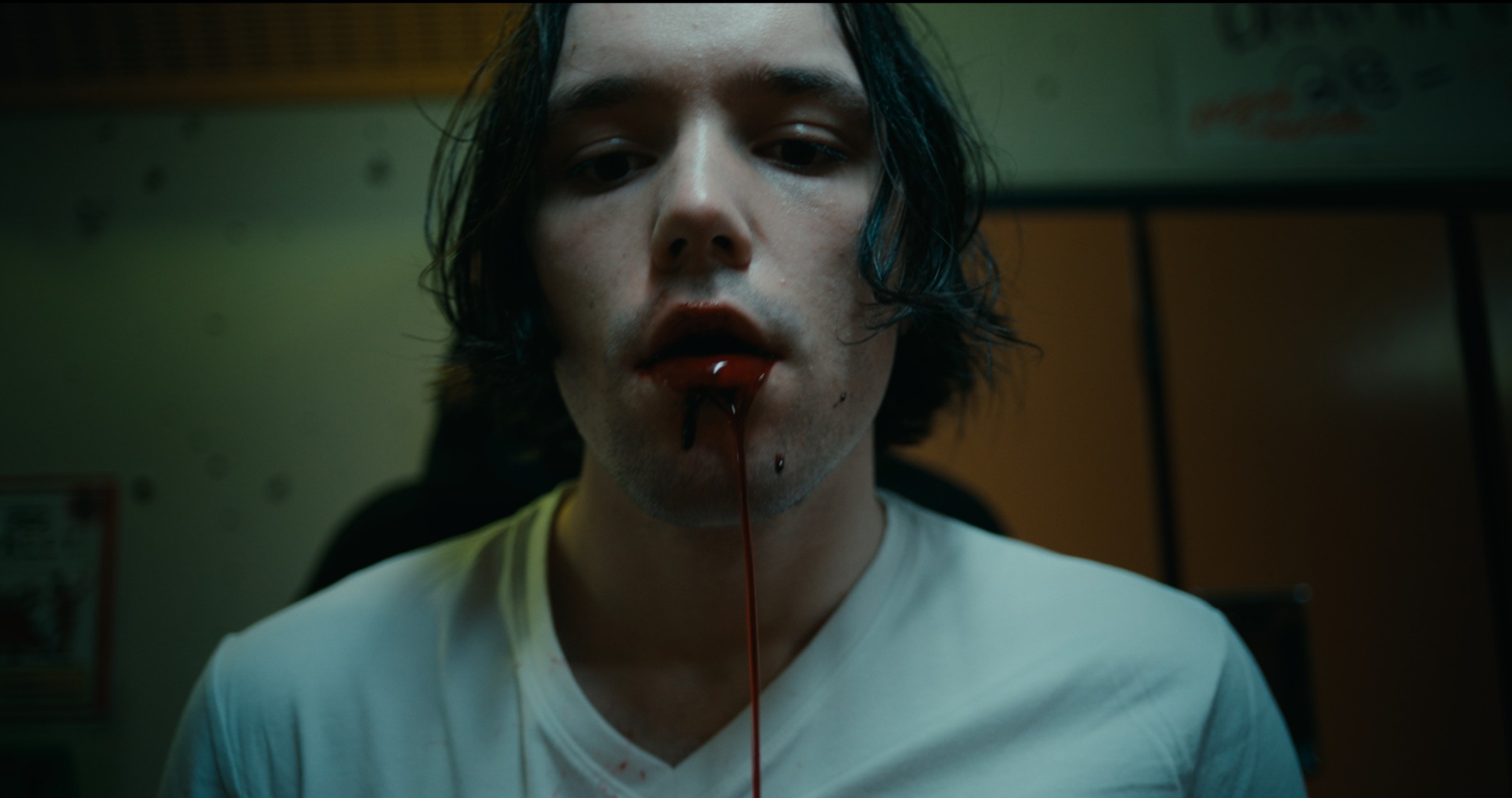 A pale man in a white shirt looks ahead in a dim room — Nemesis