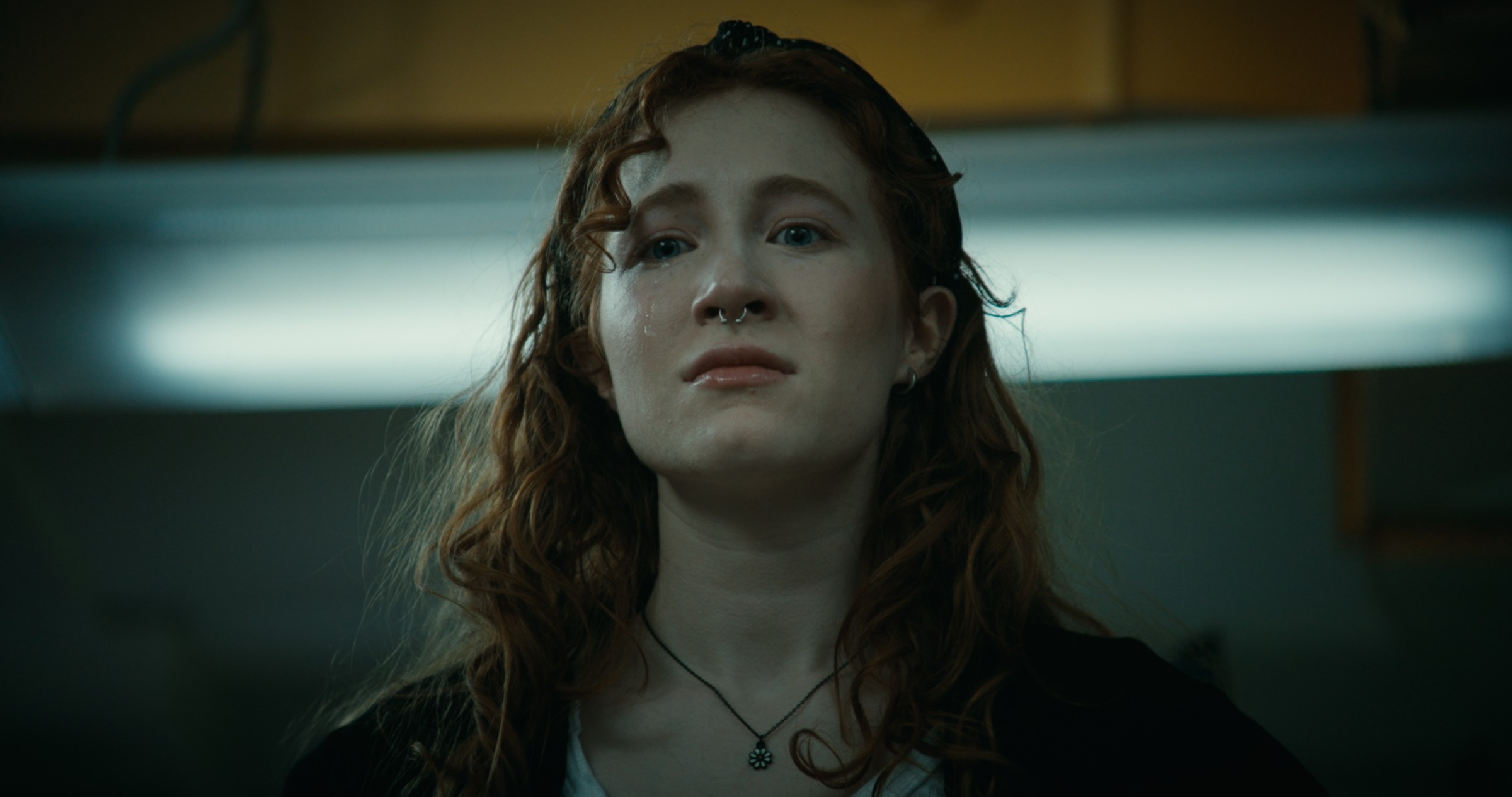 A woman looks ahead beneath a cool overhead light — Nemesis