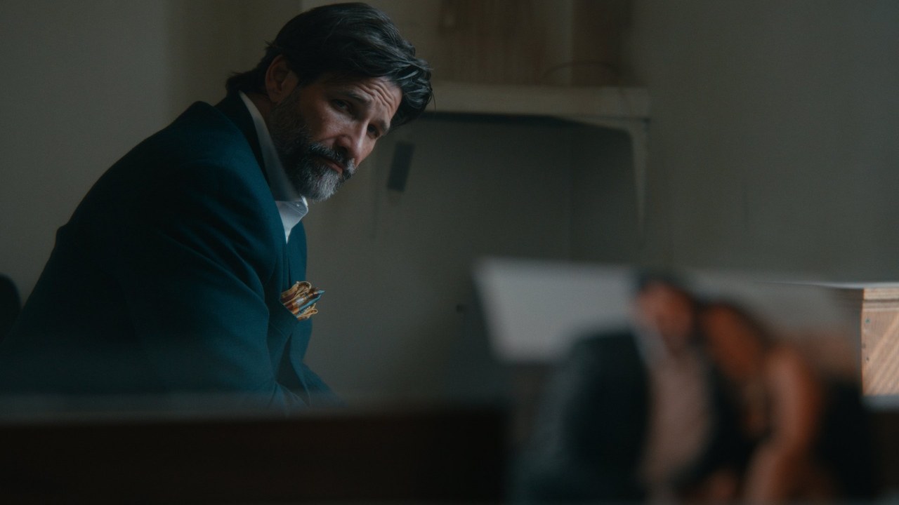 A bearded man seated in a dim, cool-toned interior from Crossroads