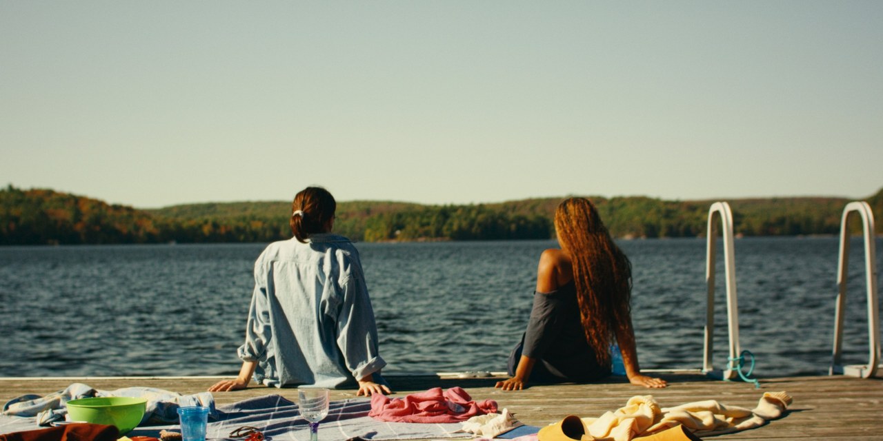 Two friends seated on a dock facing the lake in Girls Weekend