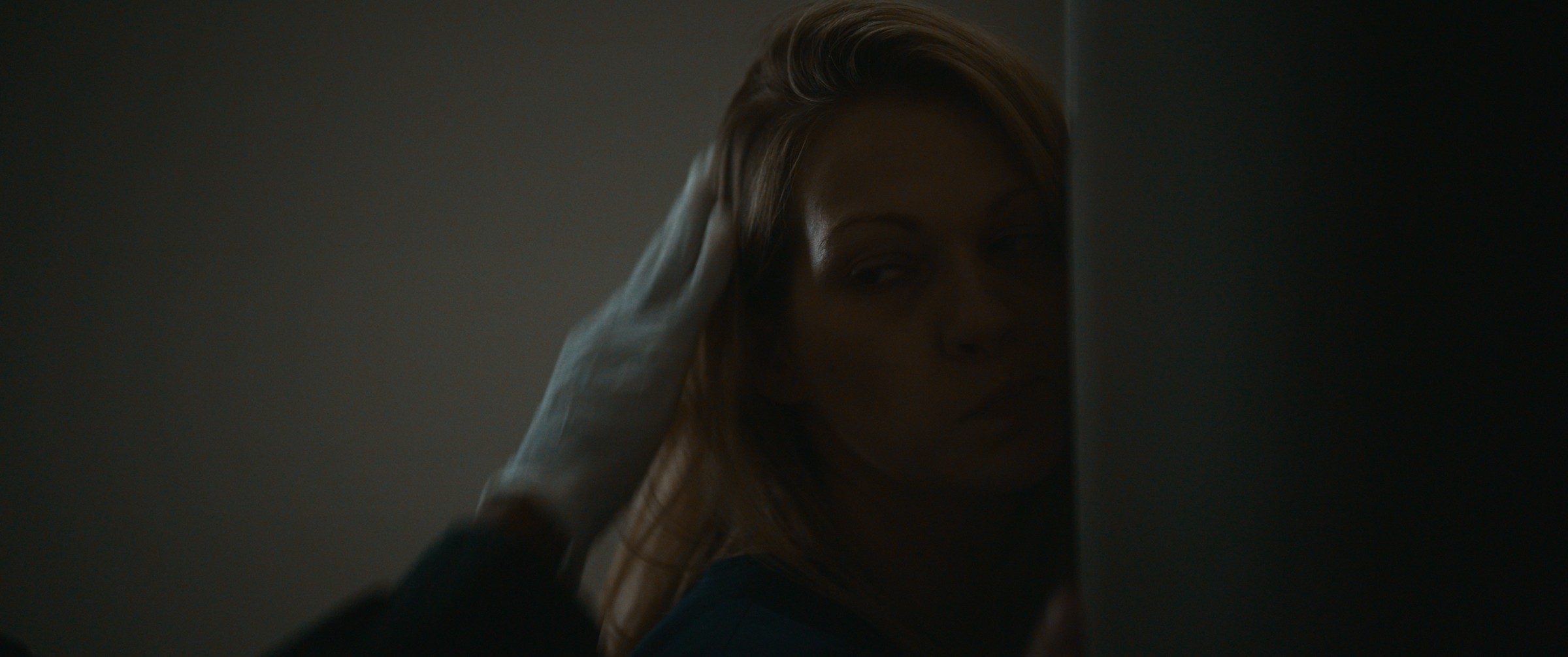 A woman rests her hand against her head in a dim room — The Table Between Us