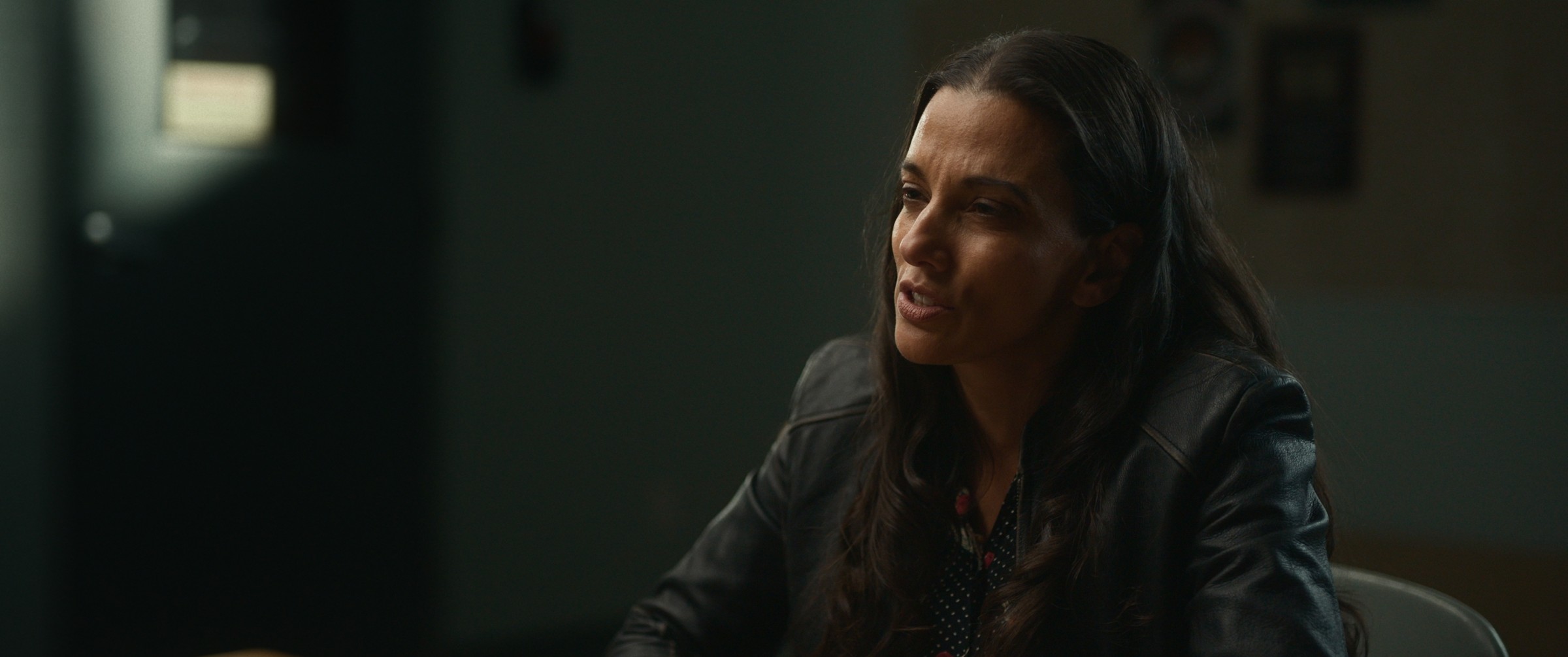 A woman speaks across a table in a dim room — The Table Between Us