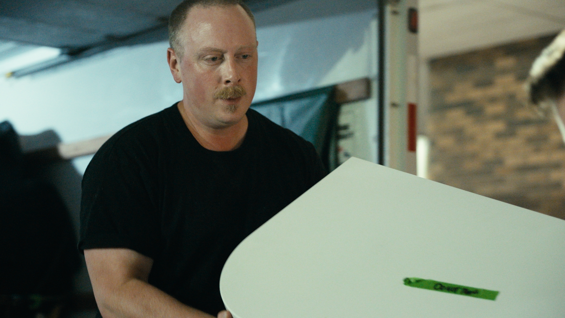 A man carries a white display panel beside a truck — Time Store