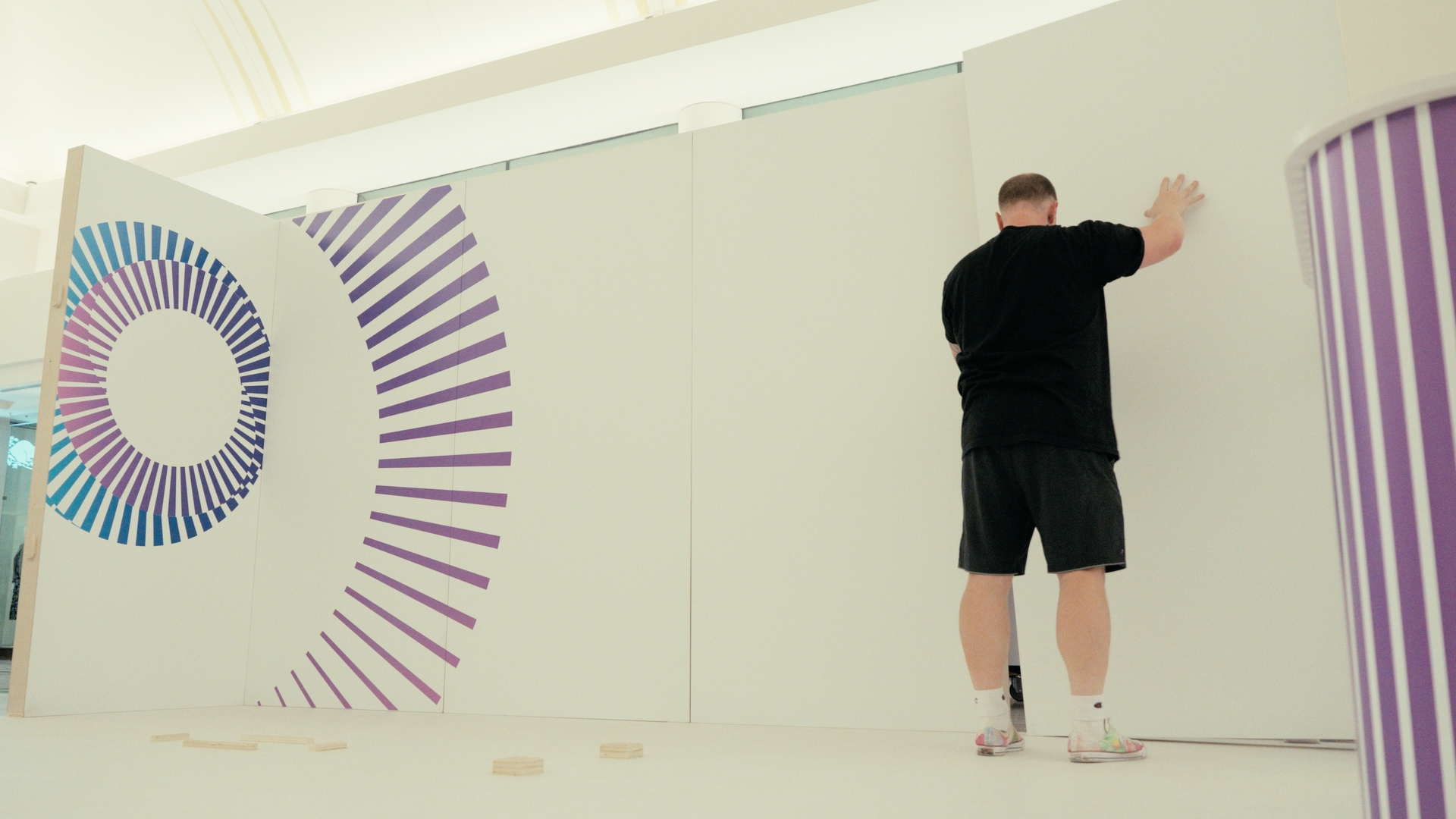 A worker installs a white wall with purple circular graphics — Time Store