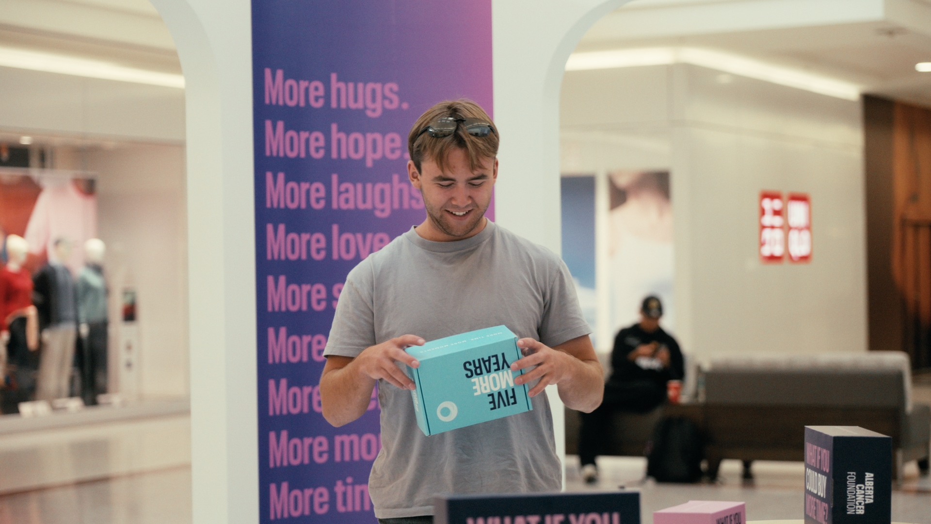 A smiling man holds a turquoise box beside a purple sign — Time Store