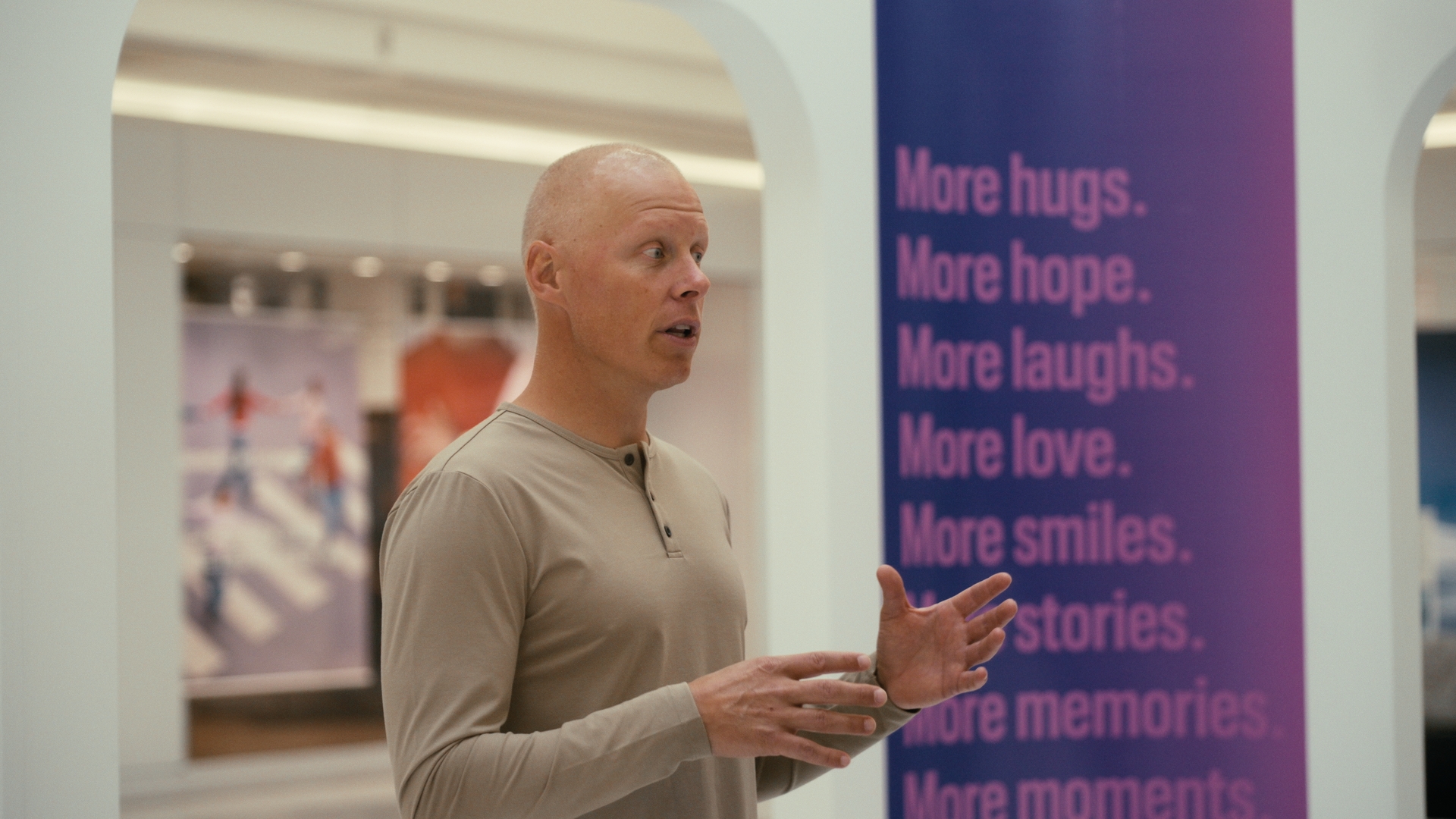 A man speaks while holding his hands beside a purple sign — Time Store