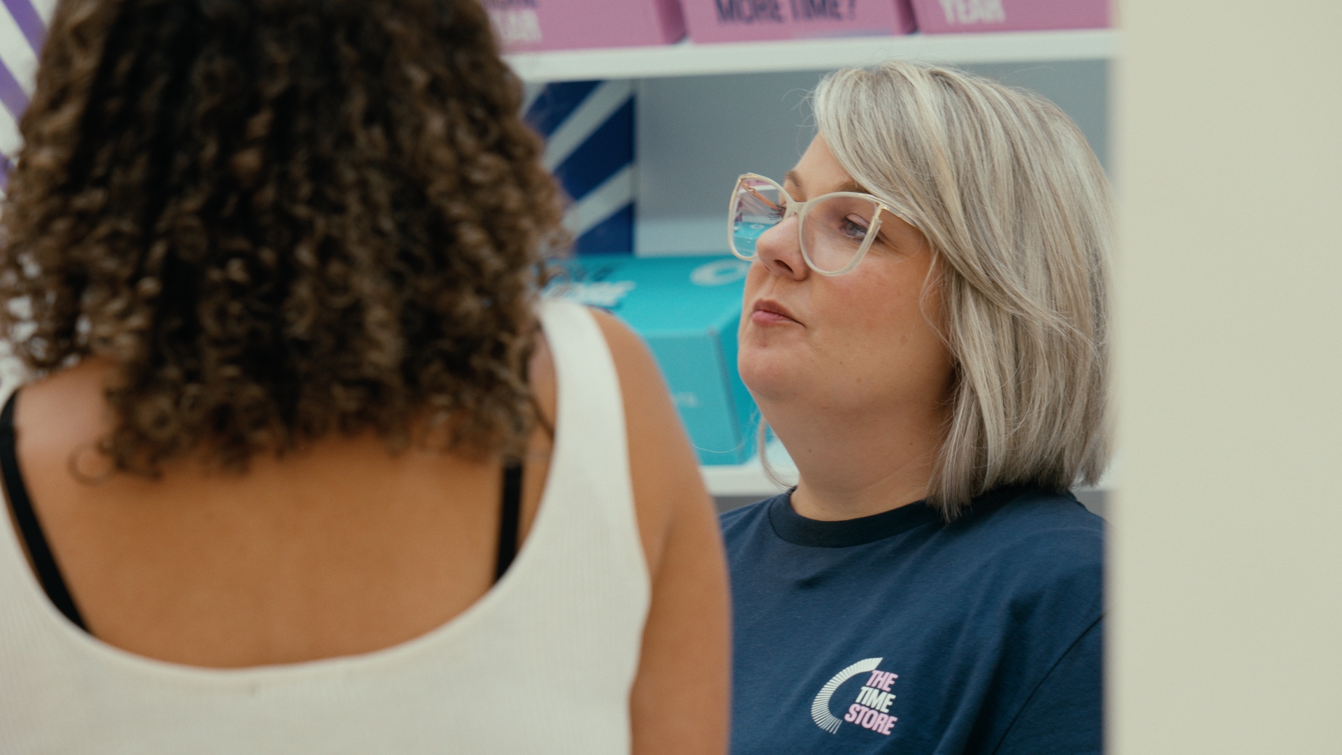 A woman with glasses talks to another visitor beside a display — Time Store