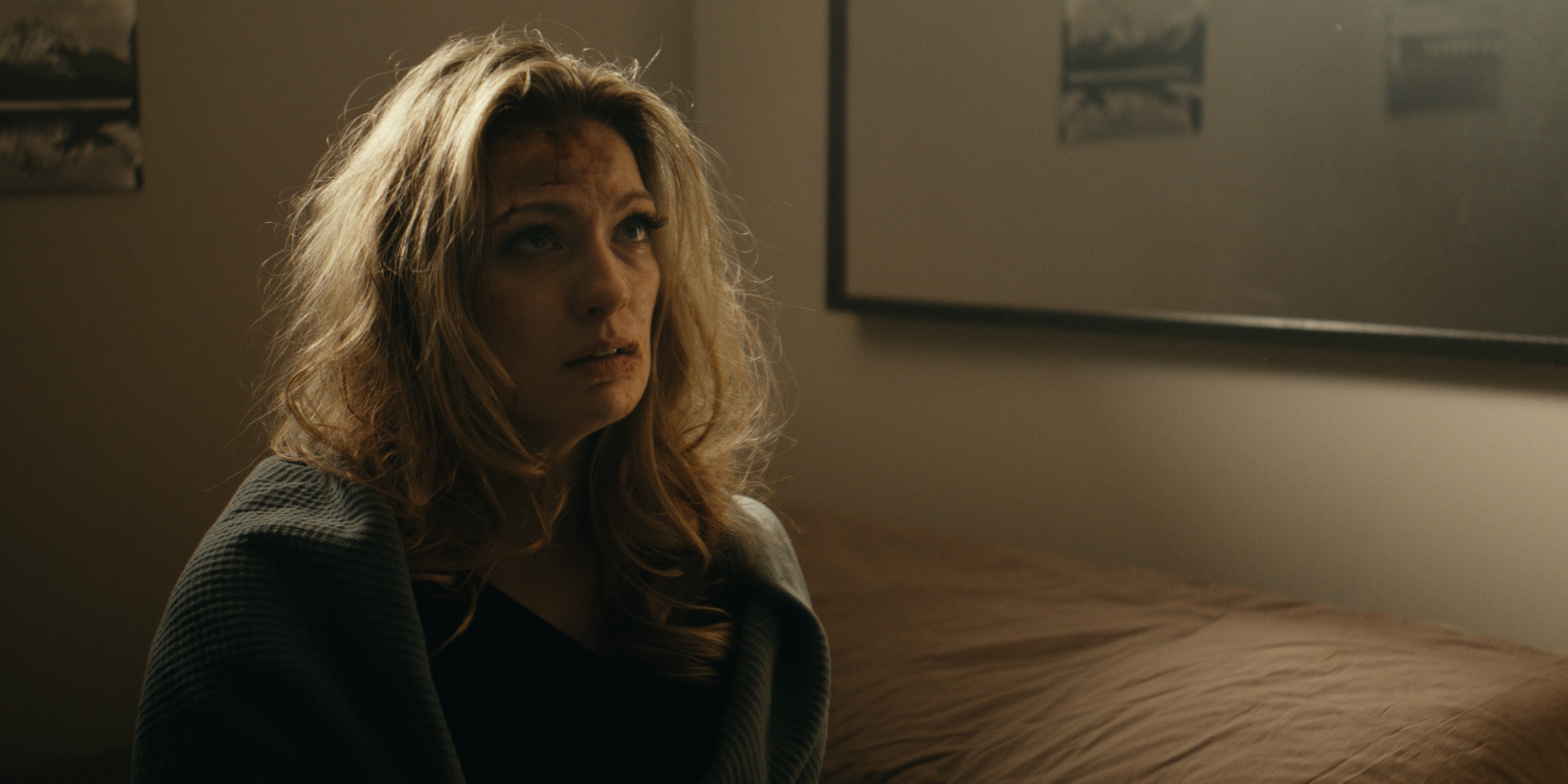 A woman wrapped in a blanket sits beside a bed — Trinkets
