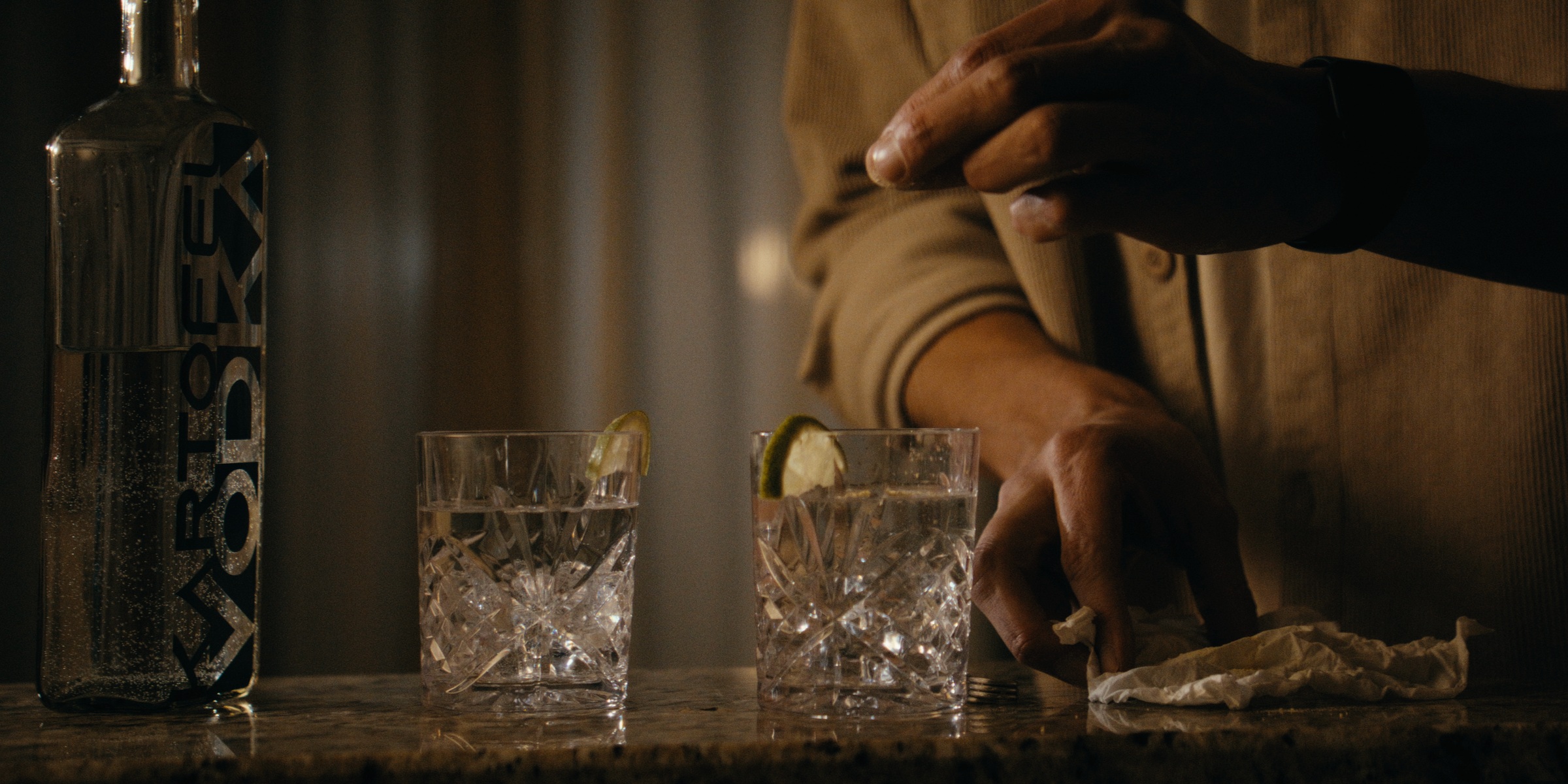 Hands beside a bottle and two glasses on a table — Trinkets