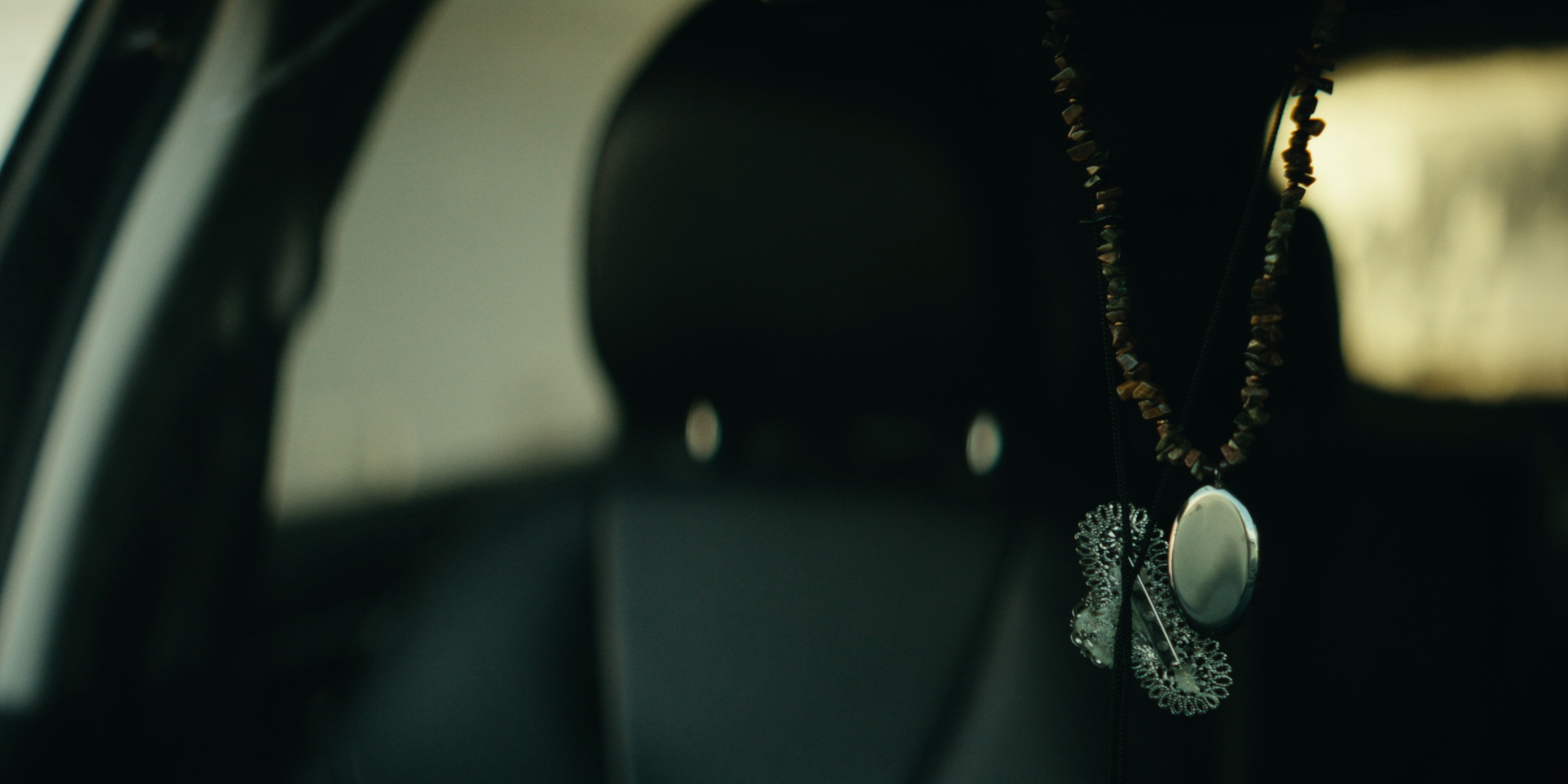 A pendant hangs inside a car beside a dark headrest — Trinkets
